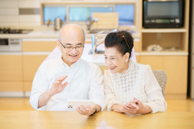 自宅でスマートフォンを見ながら笑顔で話すご夫婦